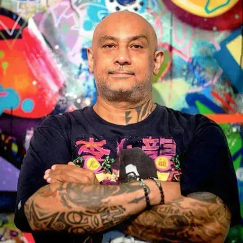 Bald man with tattoos in black t-shirt featuring colorful graphics from Cope2 collection.