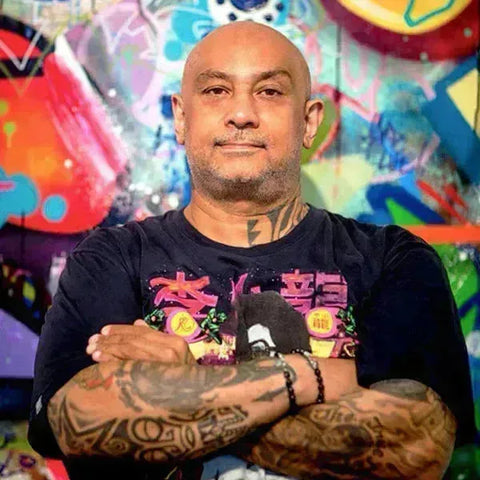 Bald man with tattoos in black t-shirt featuring colorful graphics from Cope2