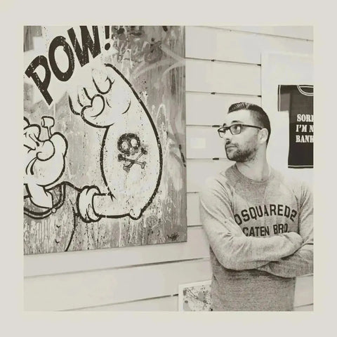 Graffiti artwork of cartoon character and POW next to man in glasses and sweatshirt.