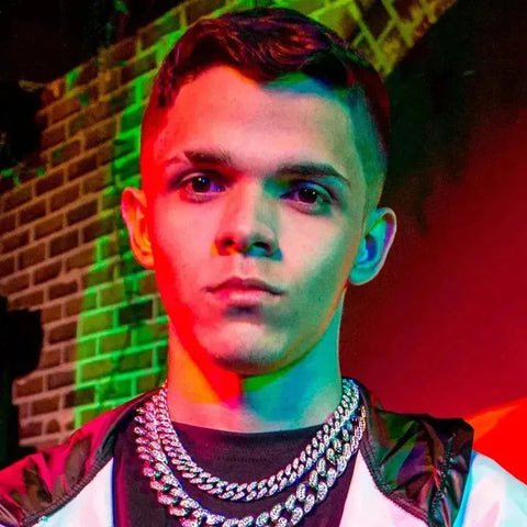 Young man with dark hair in silver chains and jacket under colorful lighting in Niack collection