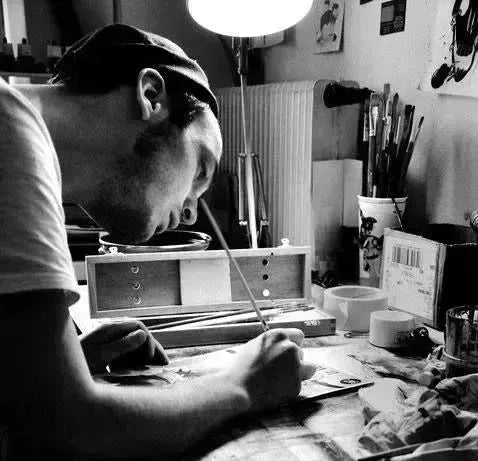 Person in cap deeply focused on task at a desk in Nicolas Blind collection.