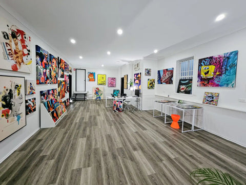 Art gallery displaying vibrant, colorful paintings and artworks on white walls.