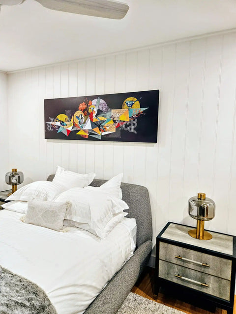 Bed with white bedding and a gray headboard beneath a colorful abstract artwork.