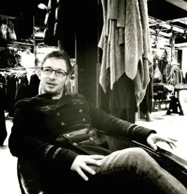 Man wearing glasses and a dark sweater sitting in a chair.