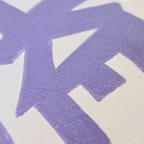 A close up of a purple painted cross on a white canvas