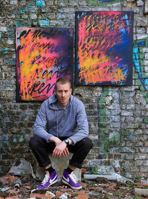 Person sitting in front of colorful abstract paintings on a stone wall.